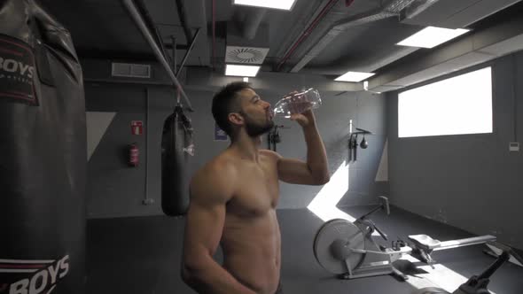 Young athletic man doing exercise at the gym taking a rest and drinking water