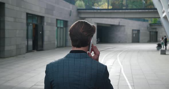 Rear View of Ambitious Businessman Talking on Mobile Phone and Walking Through the Business District