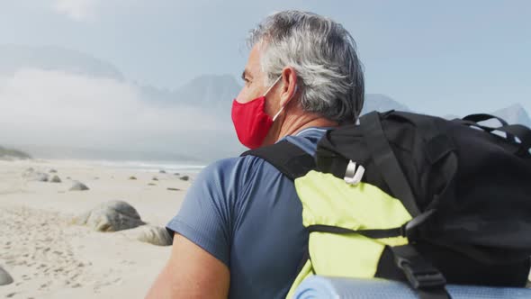 Senior hiker man wearing face mask with backpack walking while hiking on the beach.