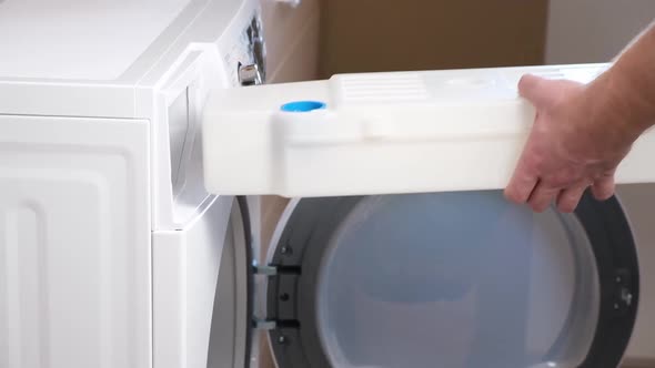 A Man Takes Out a Container From Dryer to Collect Water Squeezed Out of Wet Laundry