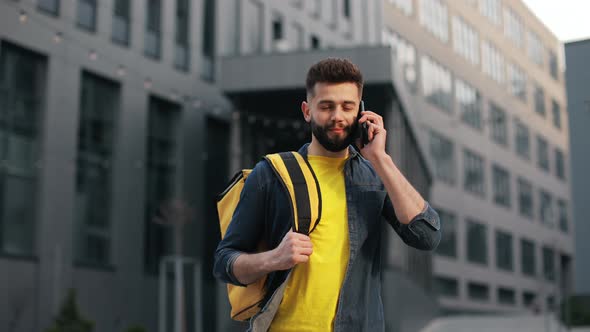 The Food Delivery Guy is Standing and Talking on a Smartphone