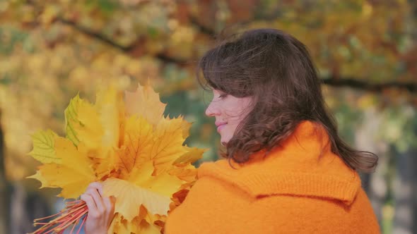 Young Beautiful Woman Playing with Autumn Leaves in Fall Park