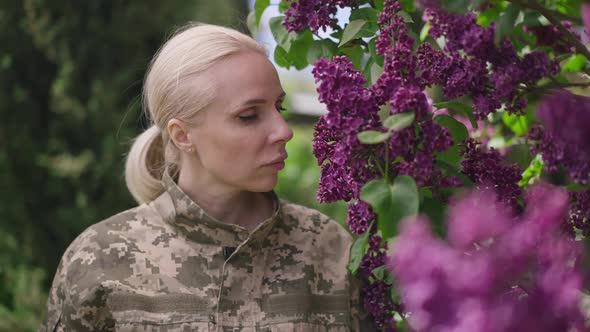 Beautiful Blond Female Soldier Smelling Flowers on Tree Branch and Looking at Camera