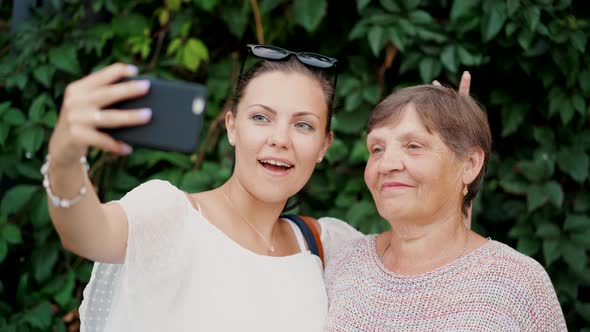 Pretty Old Granny and Her Granddaughter Doing Selfie Outdoor Fooling Around Looking at Camera 