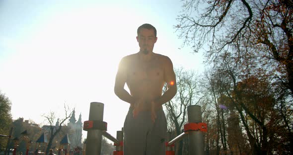 Young Man Is Doing Push-ups on Bars with Clapping His Arms in Good Weather 