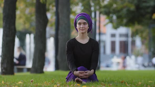 Beautiful Muslim Young Islamic Girl in Purple Hijab Female Buddhist Sits on Green Grass Lawn in City