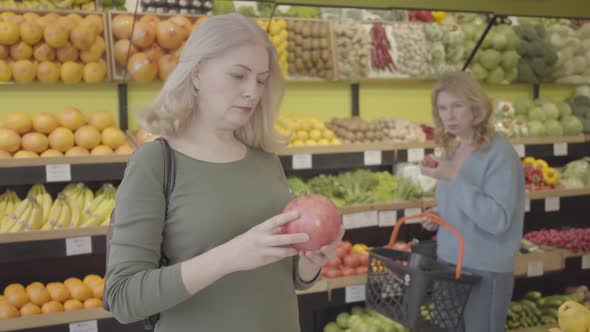 Portrait of Mature Caucasian Woman Advising with Friend on Purchase of Juicy Organic Pomegranate