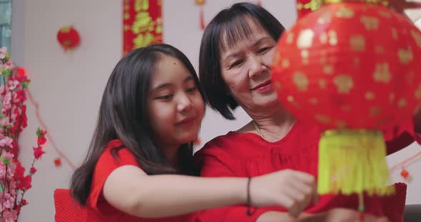 Asian Senior Woman And Niece Decorate House For Chinese New Year Celebrations With Flowers.