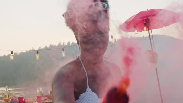 Happy Black Woman Dancing with Colored Smoke Bomb at Summer Party