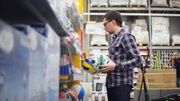 A Man Looks at Volleyball and Soccer Balls in a Hypermarket for a Sports Game