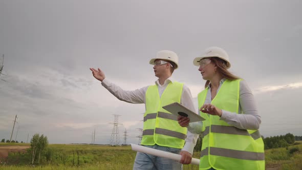 An Electrician Male and Female in the Fields Near the Power Transmission Line