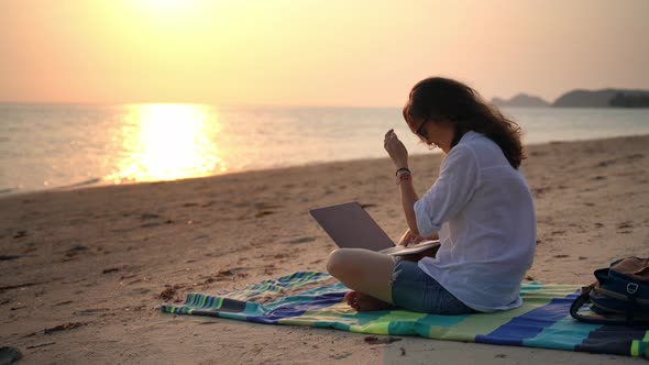 A Young Woman Writer Sitting on the Beach with Her Laptop and Typing a Text.