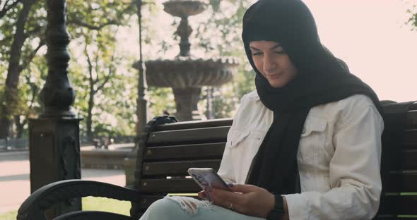 Muslim Woman Holding Smartphone in City Park