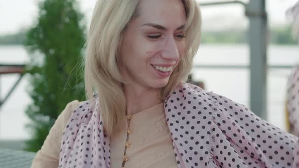 Close-up of Charming Blond Woman with Brown Eyes Putting on Light Summer Scarf. Portrait of Happy