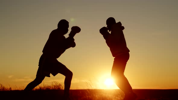 Silhouette Two AfricanAmericans Man are Training to Boxing Against Background of Sunset Side View