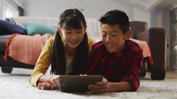 Asian brother and sister smiling and using tablet at home