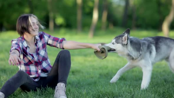 Beautiful Young Woman Playing with Funny Husky Dog Outdoors in Park at Sunset or Sunrise on Green