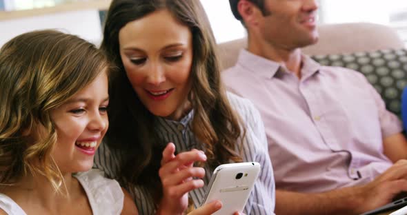 Mother and daughter using mobile phone in living room