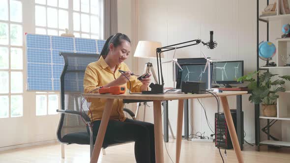 Asian Woman With Wind Turbine Fix The Circuit Board While Working With Laptop Next To The Solar Cell