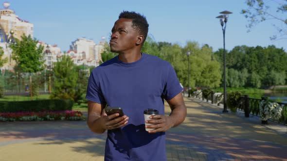 Thoughtful AfroAmerican Man Walks Street Looks Around Smartphone Navigator