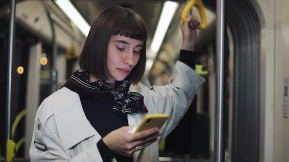 Portrait of Young Hipster Woman Holds the Handrail Using Smartphone Standing in Public Transport