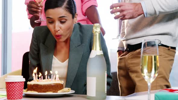 Businesswoman blowing birthday candles with colleagues