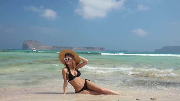 beautiful young woman in straw hat and swimsuit relaxing sitting on beach