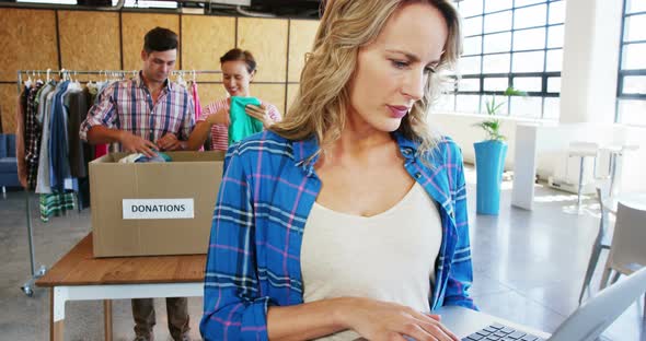 Woman working on laptop while volunteers sorting clothes in the background