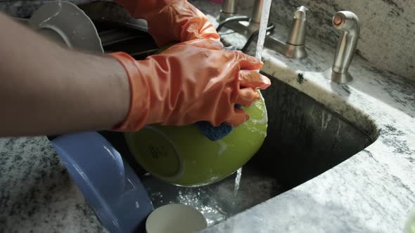 Close Up View of Hands in Orange Gloves Wash Dishes in the Kitchen