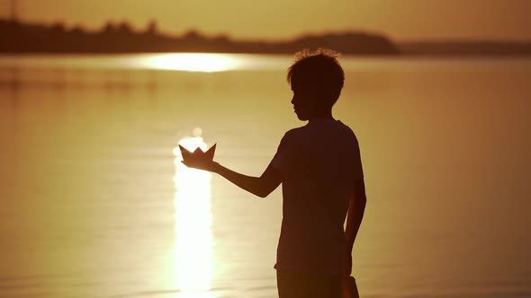 Boy with Red and green Paper Ships is standing in the river. Origami Paper Boat in kid's hands. 