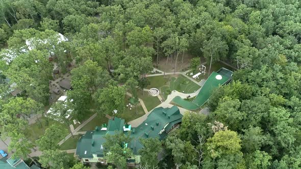 Top view of a complex of houses with a green tiled roof in the middle of a forest on a summer 