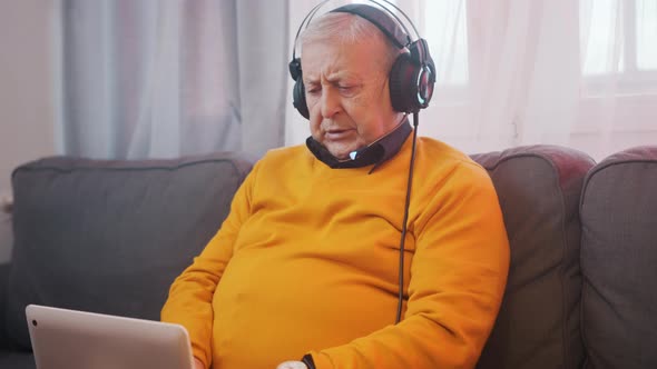 Portrait of Elderly Man with Headset Playing Games on the Laptop