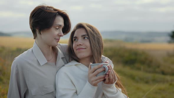 Couple of Two Loving Women Sitting on Nature with Hot Drinks