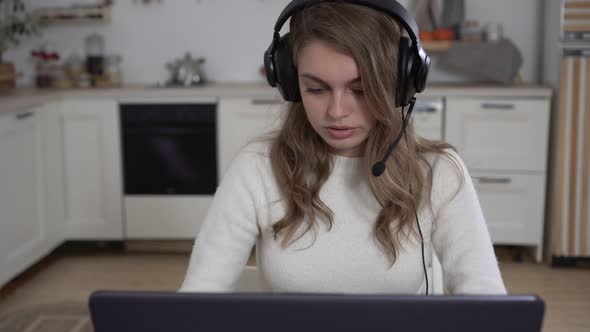 Young Woman at Home with a Laptop in Headphones with a Microphone