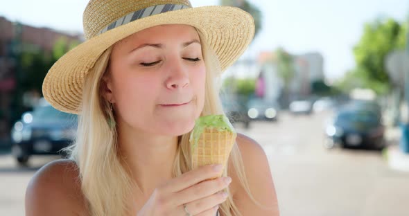 Young Blonde Woman Eating Green Mint Italian Gelato Ice Cream in Street Cafe,  alt