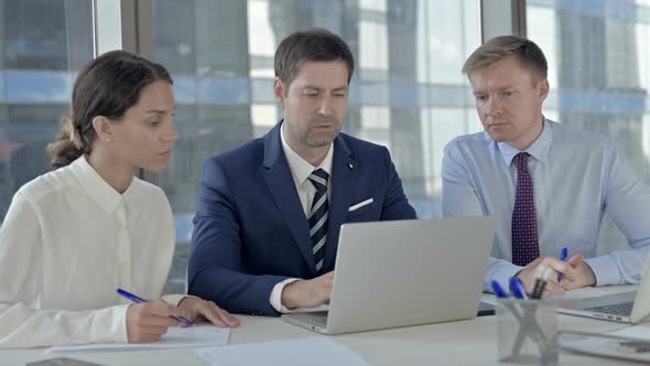 Middle Aged Businessman Using Laptop and Explaining To His Assistants on Office Table