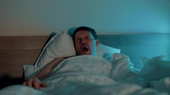 Young Man Under Blanket Sleeping on Bed in Evening