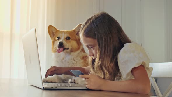 Child Working on Her Laptop at Home and Do Some Operation With a Credit Card. Modern Education