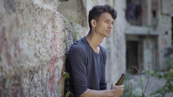 Side View of Desperate Gypsy Man Drinking Beer at Urban Slums. Portrait of Depressed Young Guy with