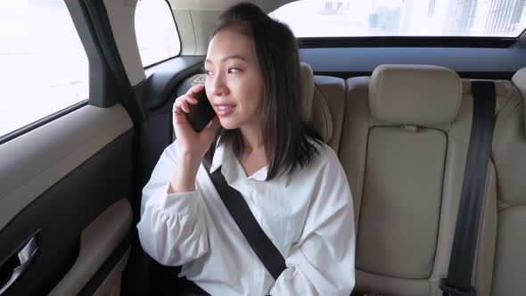 Tranquil asian woman having phone call on backseat in car