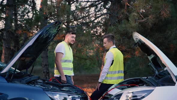 Two Men in a Green Safety Vest are Talking to Each Other Recharging Battery on the Road