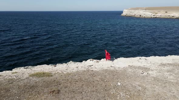 Brunette Woman in a Red Long Dress Walk on the Edge of a Cliff By the Sea