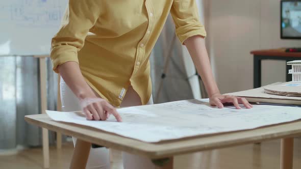 Asian Woman Engineer With A Laptop Looking At Blueprint While Working At The Office