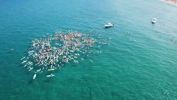 Cool overhead orbit of a large group of paddle boarders splashing.