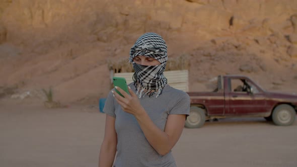 Woman Wearing Checkered Keffiyeh Standing in the Desert Using Cell Phone