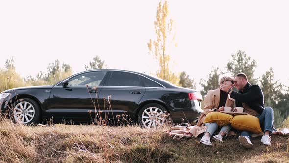 Husband and Wife Sitting Near Car Drinking Tea