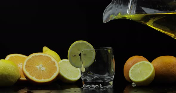 Pour Juice From Pitcher Into Glass, Orange and Lemon Slices on Background