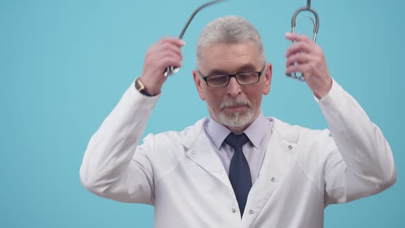 Adult doctor man in glasses and uniform puts a stethoscope around neck looking at the camera.