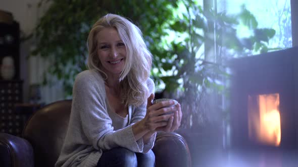 Mature woman drinking coffee in front of the fireplace