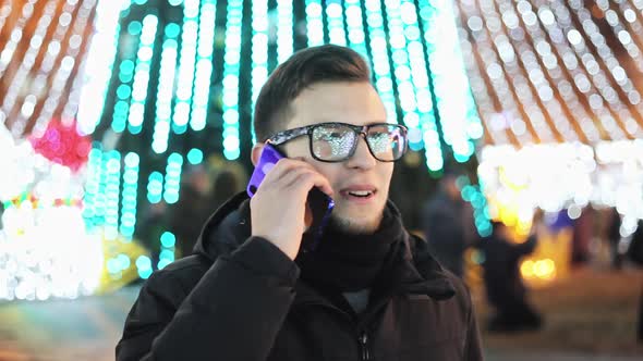 Stylish Man Talking on the Phone on Christmas Night on the Street Decorated with Festoons